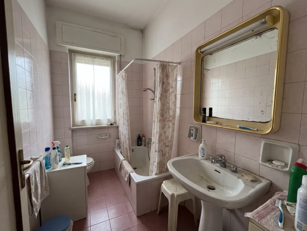 Bagno anni '80 con piastrelle rosa e fughe consumate